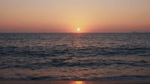 The Sun sets on a tropical sandy beach while young boy surfs the waves Stock Footage 119120279