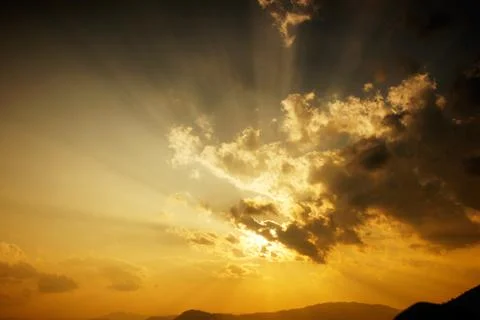 Sun setting behind the clouds and a silhouette of mountains at nightfall. Stock Photos