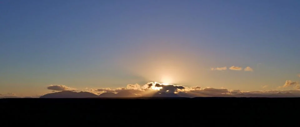 Sun Setting Behind Clouds over Darkened Landscape Stock Photos