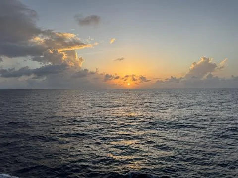 Sun Setting Behind Clouds Over Calm Ocean Horizon Stock Photos