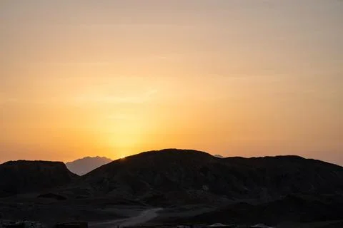 Sun setting behind dark silhouetted mountains, painting the sky with a warm.. Stock Photos