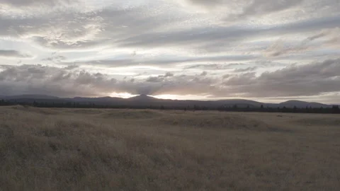 Sun setting behind distant mountain over dry grassland in rural Oregon Video stock 332308633