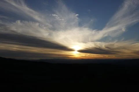Sun setting behind distant mountains creating beautiful sky Stock Photos