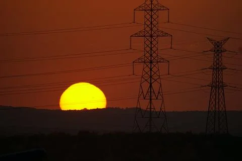 Sun setting behind electricity pylons and power lines in El Cañaveral, Madrid Stock Photos
