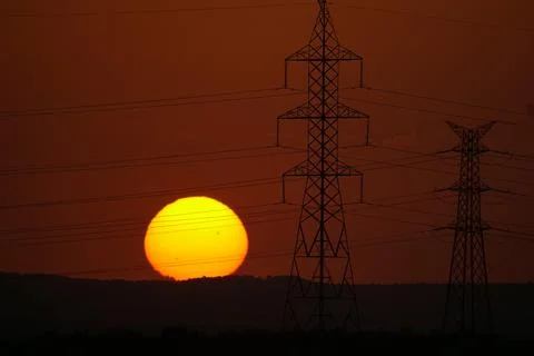 Sun setting behind electricity pylons and power lines in El Cañaveral, Madrid Stock Photos