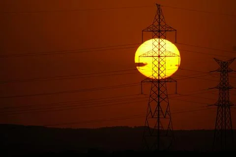 Sun setting behind electricity pylons and power lines in El Cañaveral, Madrid Stock Photos