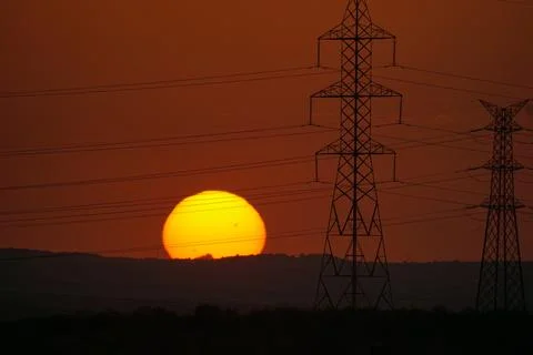 Sun setting behind electricity pylons and power lines in El Cañaveral, Madrid Stock Photos