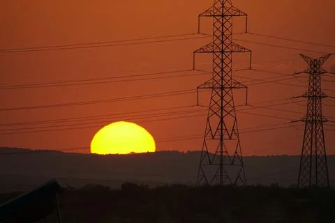 Sun setting behind electricity pylons and power lines in El Cañaveral, Madrid Stock Photos
