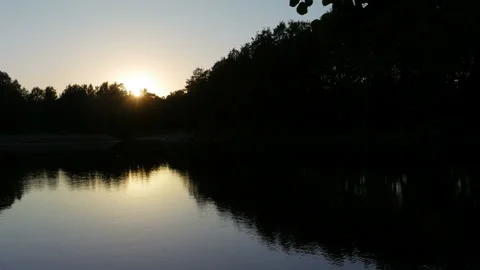 Sun setting behind forest and is reflected in the lake Stock Footage 133245097