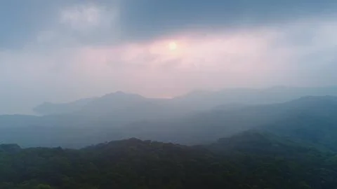 Sun setting behind misty mountains and forest aerial drone view Foto stock