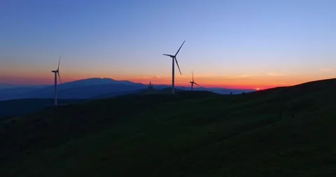 Sun Setting Behind Mountains Aerial Parallax On High Altitude Wind Turbine Farm Video stock 300486190