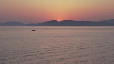 Sun setting behind the mountains on the horizon  with a small boat crossing Video stock 308044224
