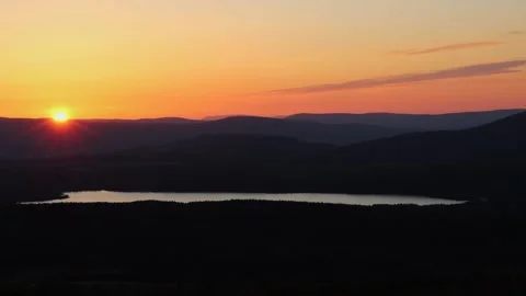 Sun setting behind mountains with Scottish loch and forest in foreground Stock Footage 310847117