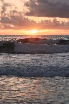 Sun setting behind the ocean with waves on the foreground Stock Photos
