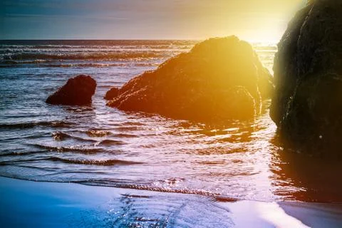 Sun setting behind rock formations in shallow water at the beach Stock Photos