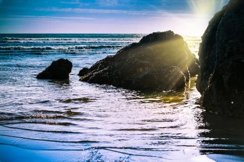 Sun setting behind rock formations in shallow water at the beach Stock Photos