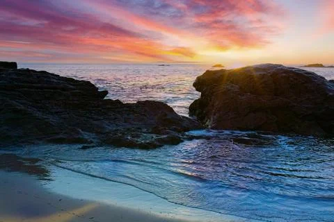 Sun setting behind rocks on the shore, Laguna Beach, California. Stock Photos
