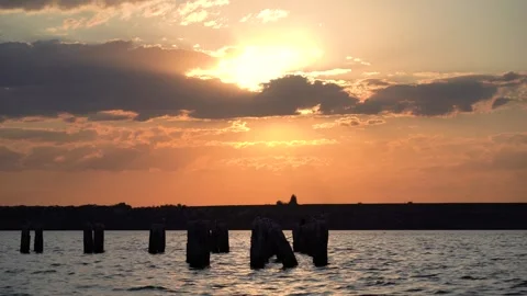 Sun setting behind scattered clouds over calm waters with silhouette Vidéo 313480886