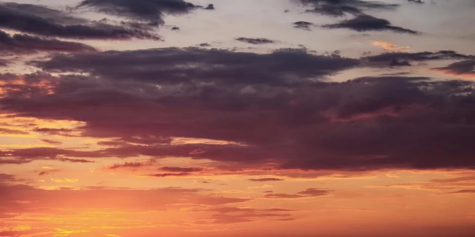The sun setting behind scattered clouds in a colorful sky. Stock Photos