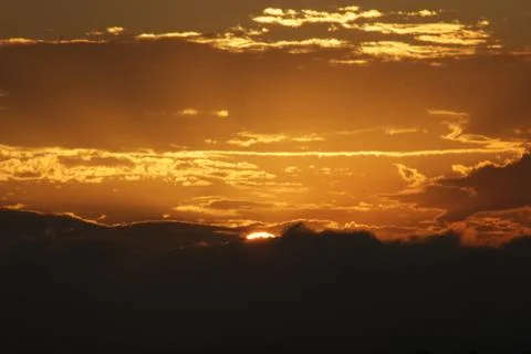 Sun setting behind silhouettes and outlines of clouds and mountain range Stock Photos