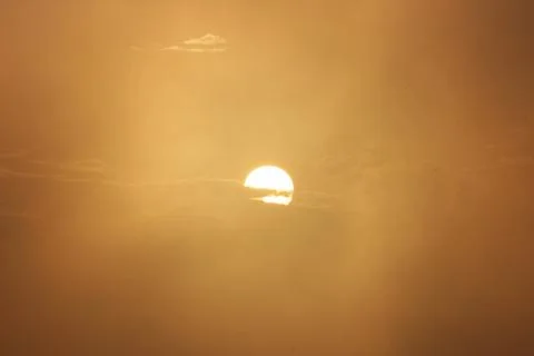 Sun setting behind slithers of clouds in foggy sky Stock Photos