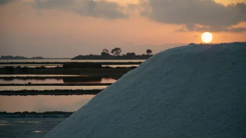 Sun setting behind a stack of salt in a salt pan 스톡 동영상 161779683