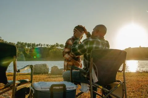 Sun setting on dad sitting in front of the lake helping his son Stock Photos