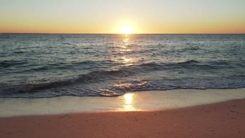 Sun setting down over the beach, calm sea waves and sand in foreground Stock Footage 153171464