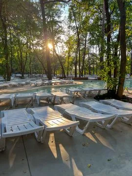 Sun setting on empty white pool loungers in lush green park Stock Photos