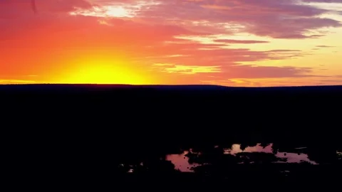 Sun setting on the horizon over the bush, reflected in a waterhole Stock Footage 345521069