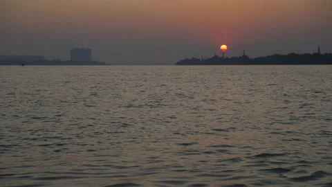 The sun is setting on the other side of the river where civilization has develop Stock Footage 222766869