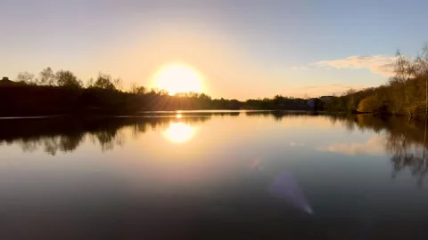 Sun Setting Over Calm Lake Surface Reflecting Light 4K 스톡 동영상 321808759