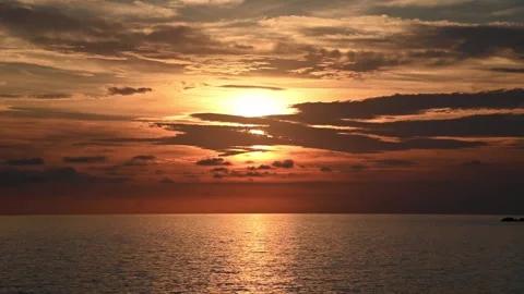 Sun setting over calm ocean horizon with golden clouds Видео 345080250