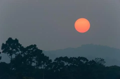 Sun setting over the mountain and tropical forest. Full sun. Massive dark spo Stock Photos