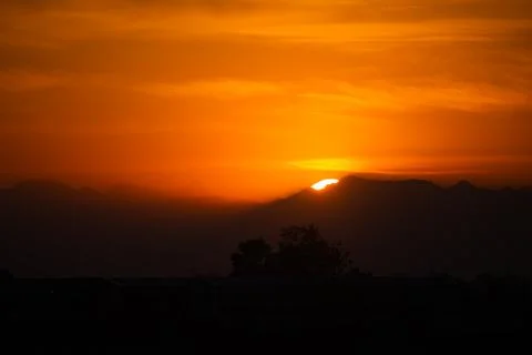 Sun Setting Over Mountain Range with Vivid Orange Sky and Shadows Foto stock