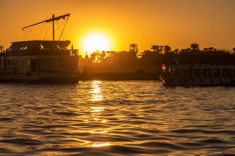 Sun setting over the Nile River in Luxor with silhouettes of ferry boats Stock Photos
