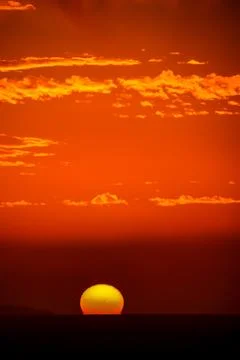 A sun is setting over the ocean, casting a warm orange glow over the water Stock Photos