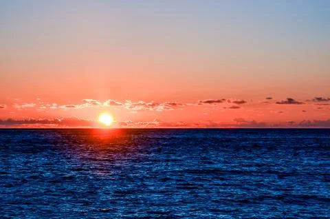 The sun is setting over the ocean, casting a warm glow on the water Stock Photos