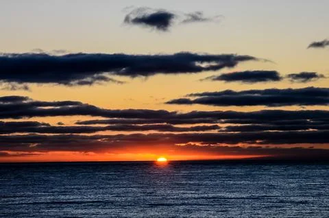 The sun is setting over the ocean, casting a warm glow on the water Stock Photos