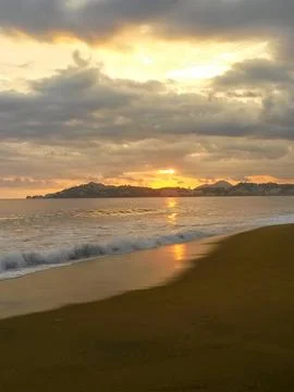 The sun is setting over the ocean, casting a warm glow over the beach Stock Photos