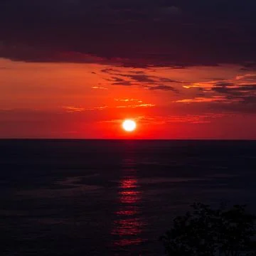 Sun setting over ocean creating dramatic red sky photo Stock Photos