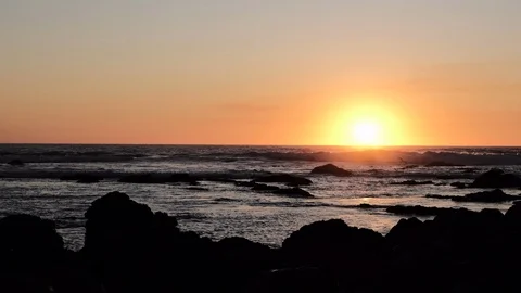 Sun setting over ocean with dark rocks in silhouette in foreground Stock Footage 115863217
