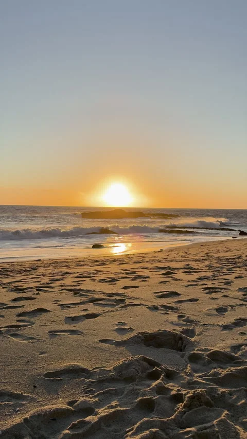 Sun setting over ocean with footprints in sand and glowing horizon Видео 331070661