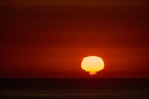 Sun setting over ocean horizon with red sky Stock Photos