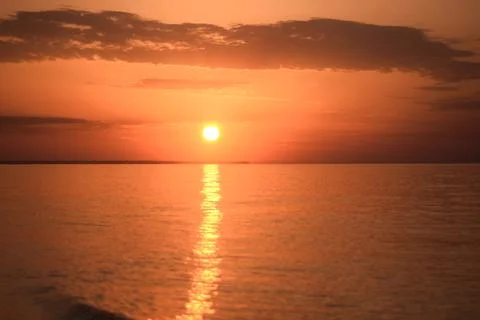 Sun setting over the ocean, reflecting a golden light across the calm water. Stock Photos
