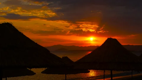 Sun setting over ocean with umbrellas on beach Vidéo 334776664