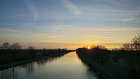 The sun is setting over a river with trees in the foreground Mittellandkanal Stock Photos