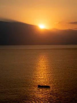 Sun setting over small boat in sea Stock Photos