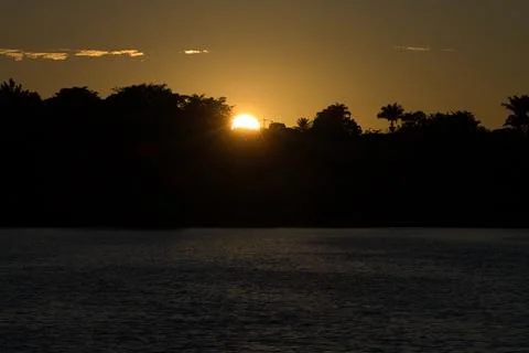 The sun is setting over the water, casting a warm glow over the trees Stock Photos