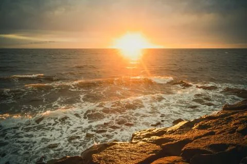 Sun setting over water with waves and rocks Stock Photos